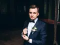Elegancki mężczyzna w granatowym garniturze i muszce, z butonierką. Wygląda jakby przygotowywał się do ważnego wydarzenia, a nie do palenia.