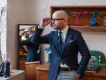 Elegancki mężczyzna w okularach dopasowuje krawat, tworząc idealny **zestaw koordynowany**. W tle widać kolorowe krawaty i poszetki.