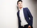 Elegancki strój wizytowy męski: granatowa marynarka, biała koszula i czarny pasek. Młody mężczyzna opiera się o ścianę, patrząc w górę.